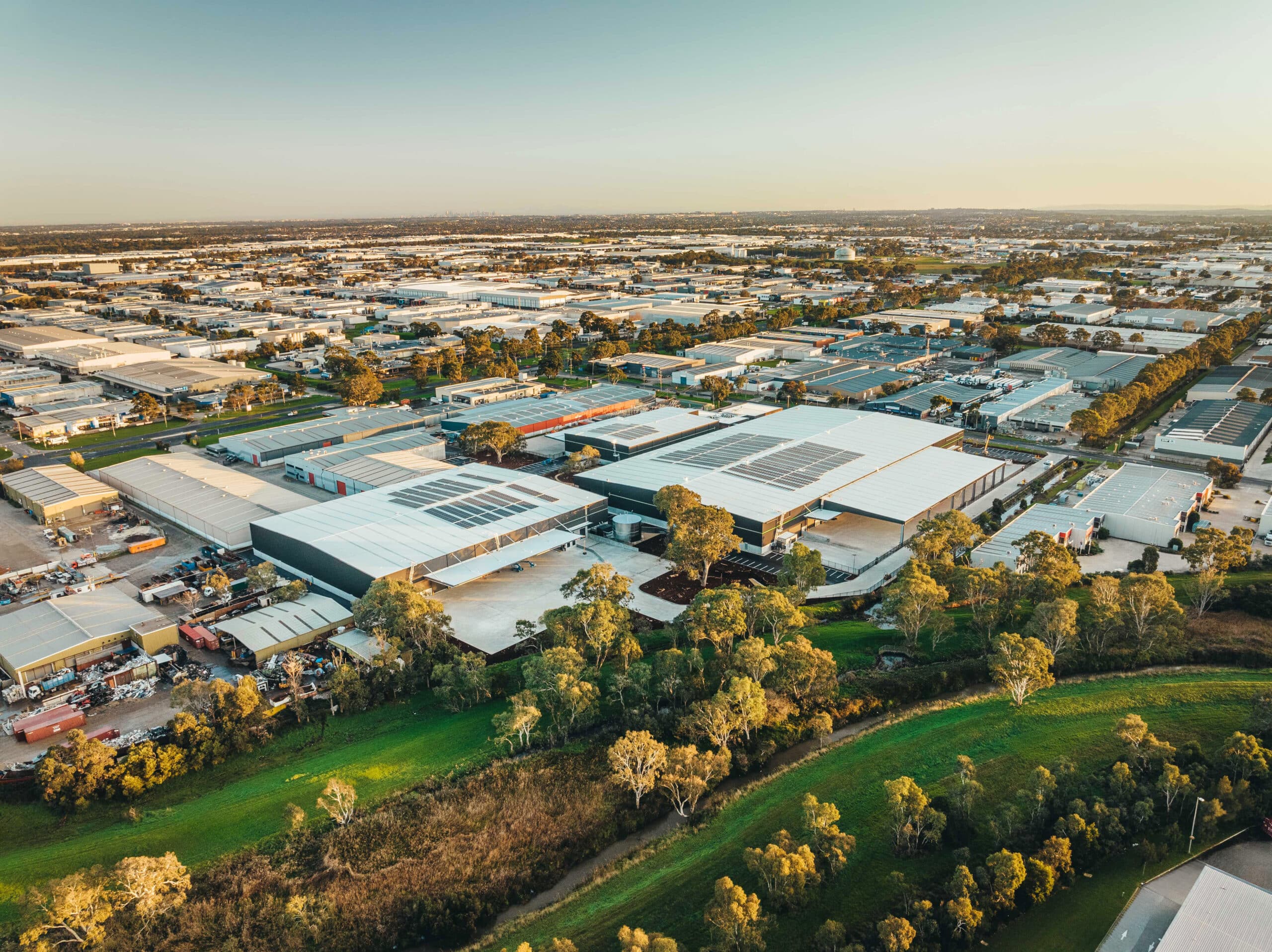 Aerial view of an industrial area with warehouses, solar panels, and surrounding green space.