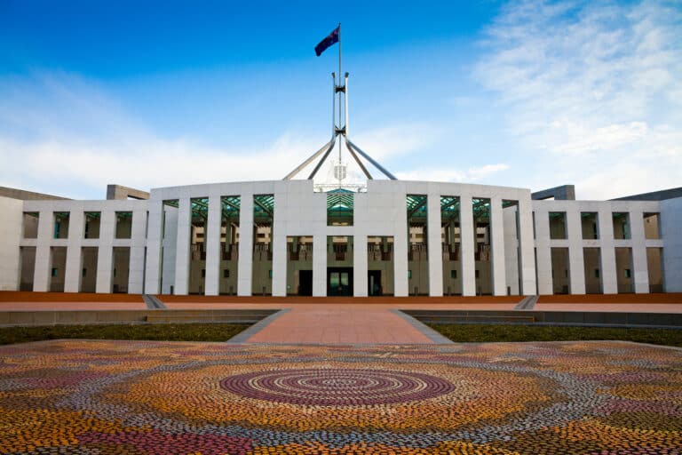 A large white building with a flag on top and an Indigenous artwork below on the ground
