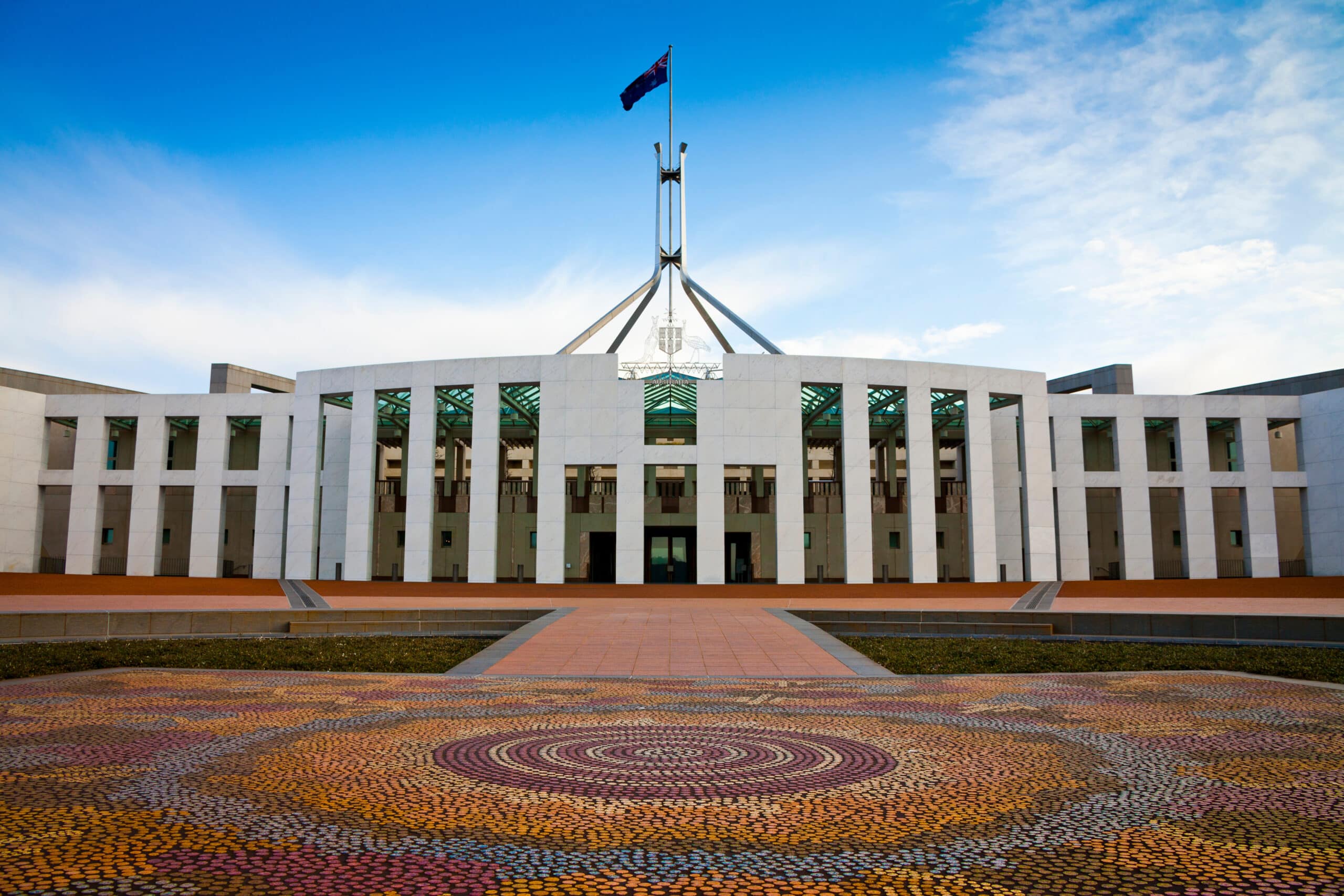 A large white building with a flag on top and an Indigenous artwork below on the ground