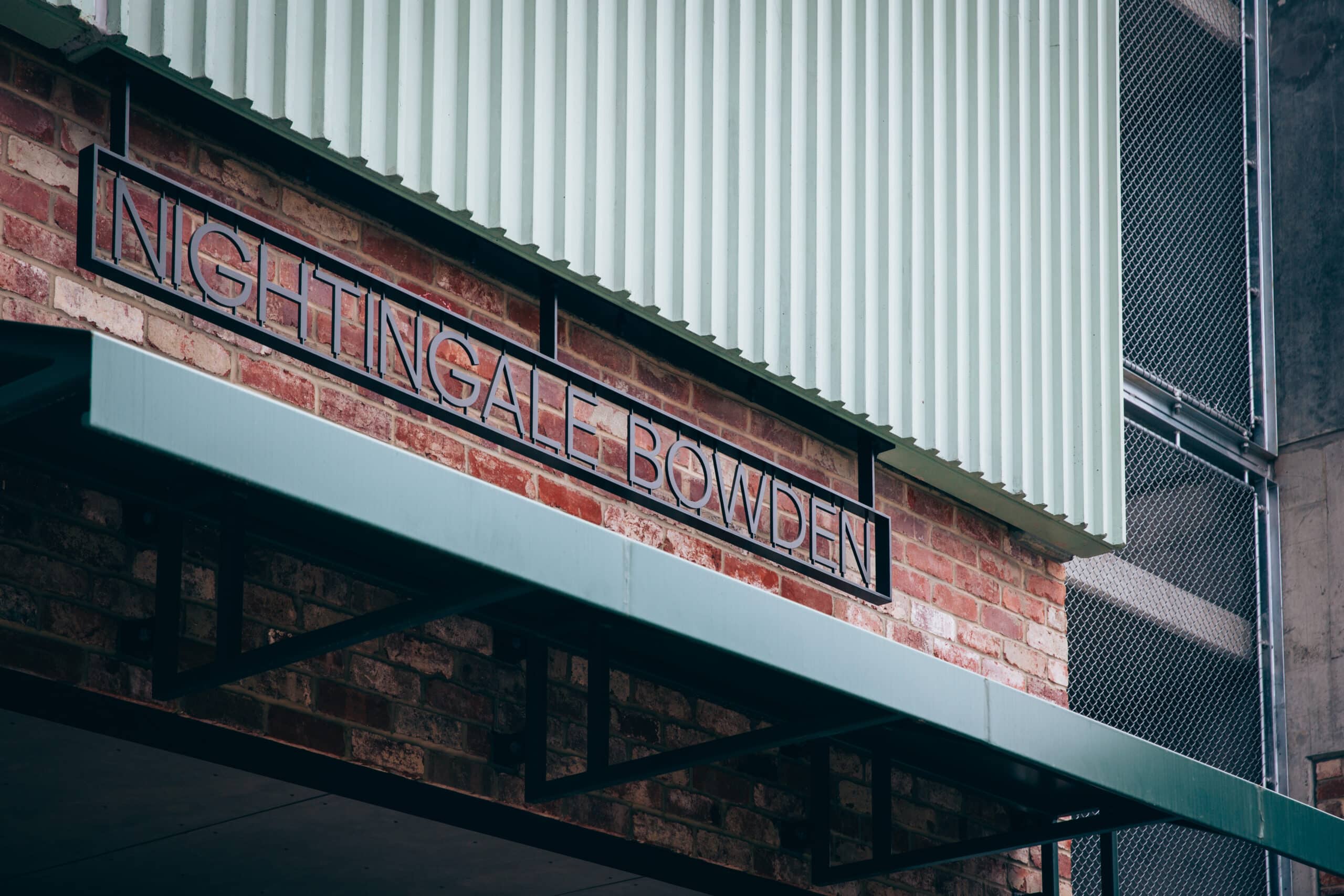 Close-up of “Nightingale Bowden” signage mounted on a brick wall beneath a corrugated metal façade and steel awning.
