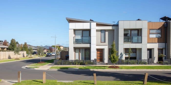 A wide shot of a white modern house on the edge of a cul-de-sac.