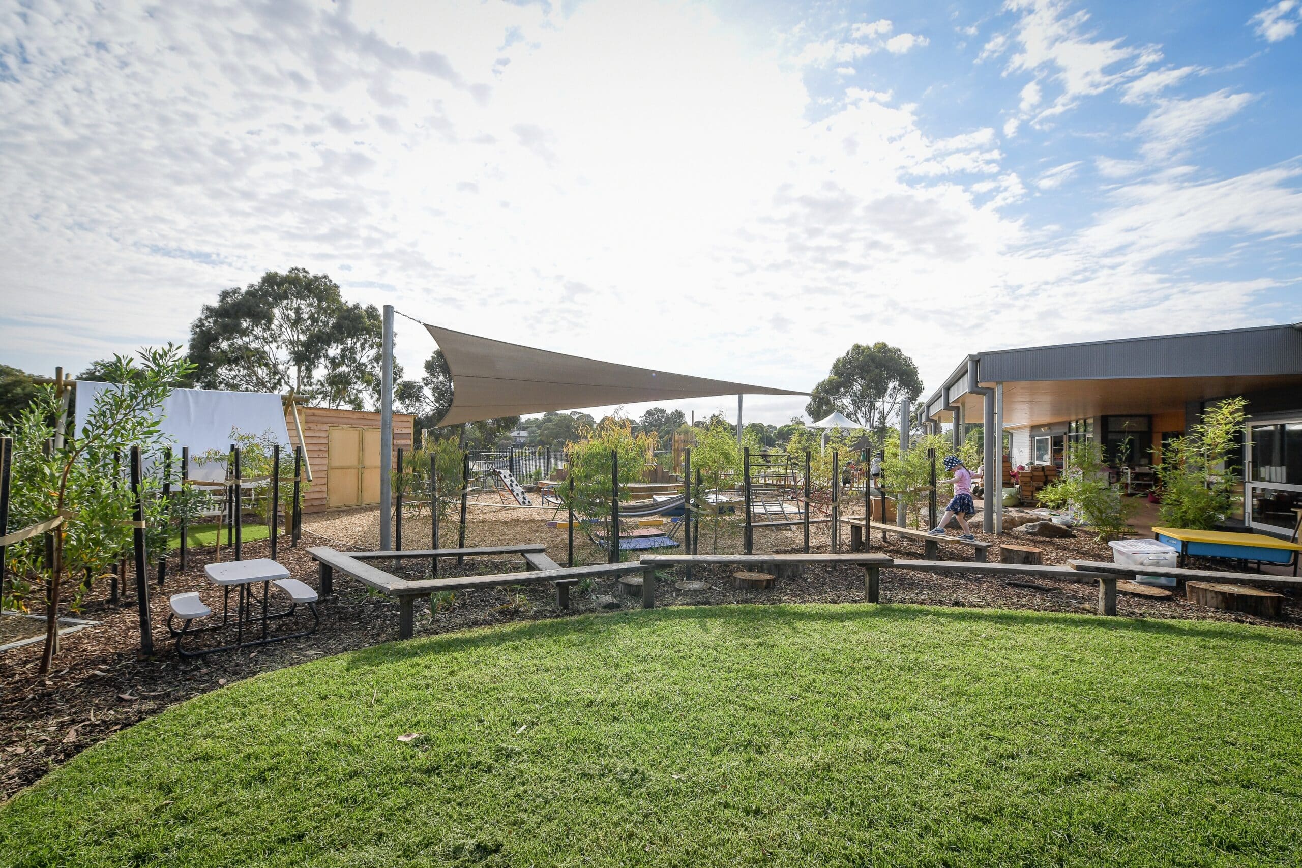 Nature-based childcare playground with outdoor learning spaces, shade structure, and landscaped early childhood education environment.