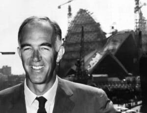 Portrait of Jørn Utzon smiling, with the Sydney Opera House under construction in the background.