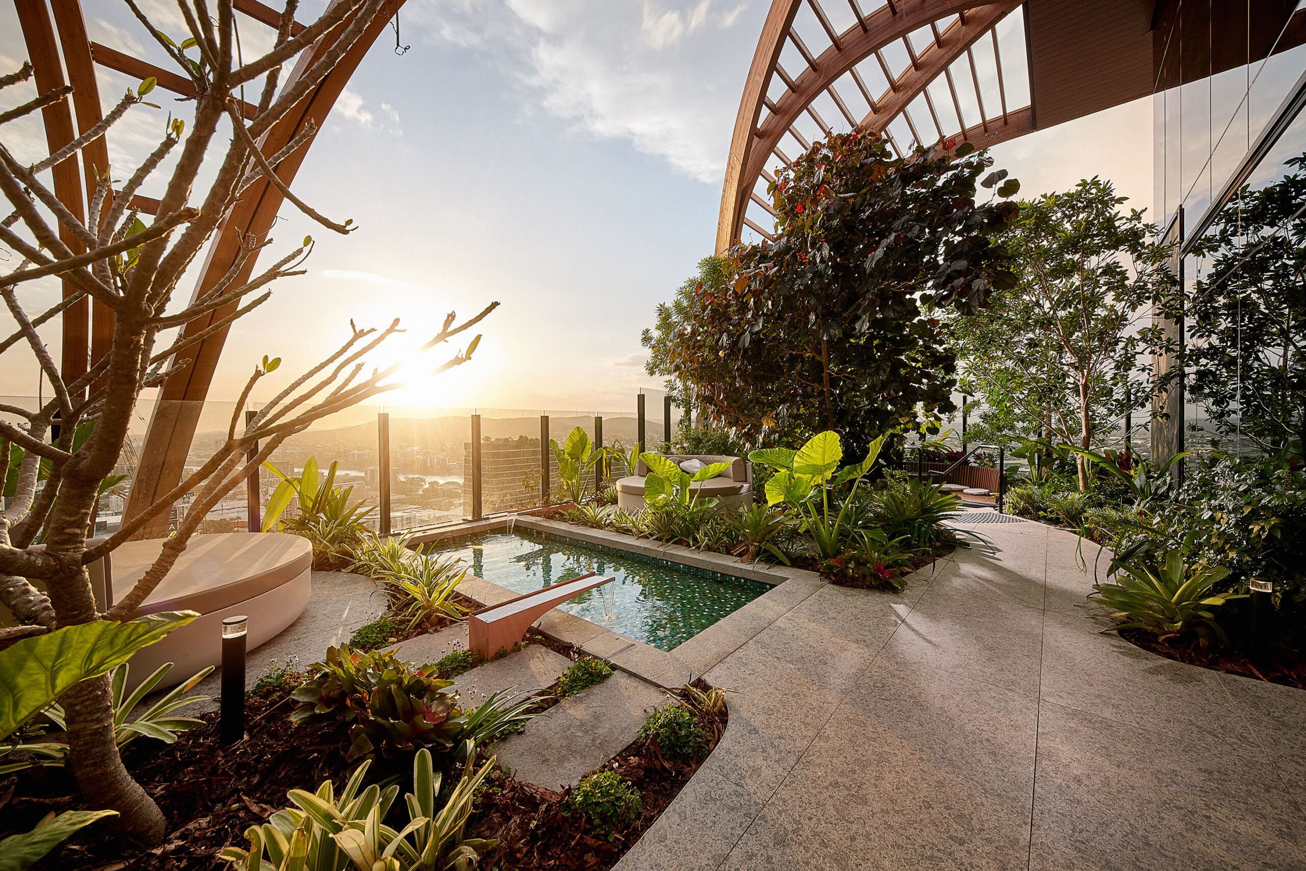 Rooftop garden terrace with a small pool, lush plants, and city views at sunset.