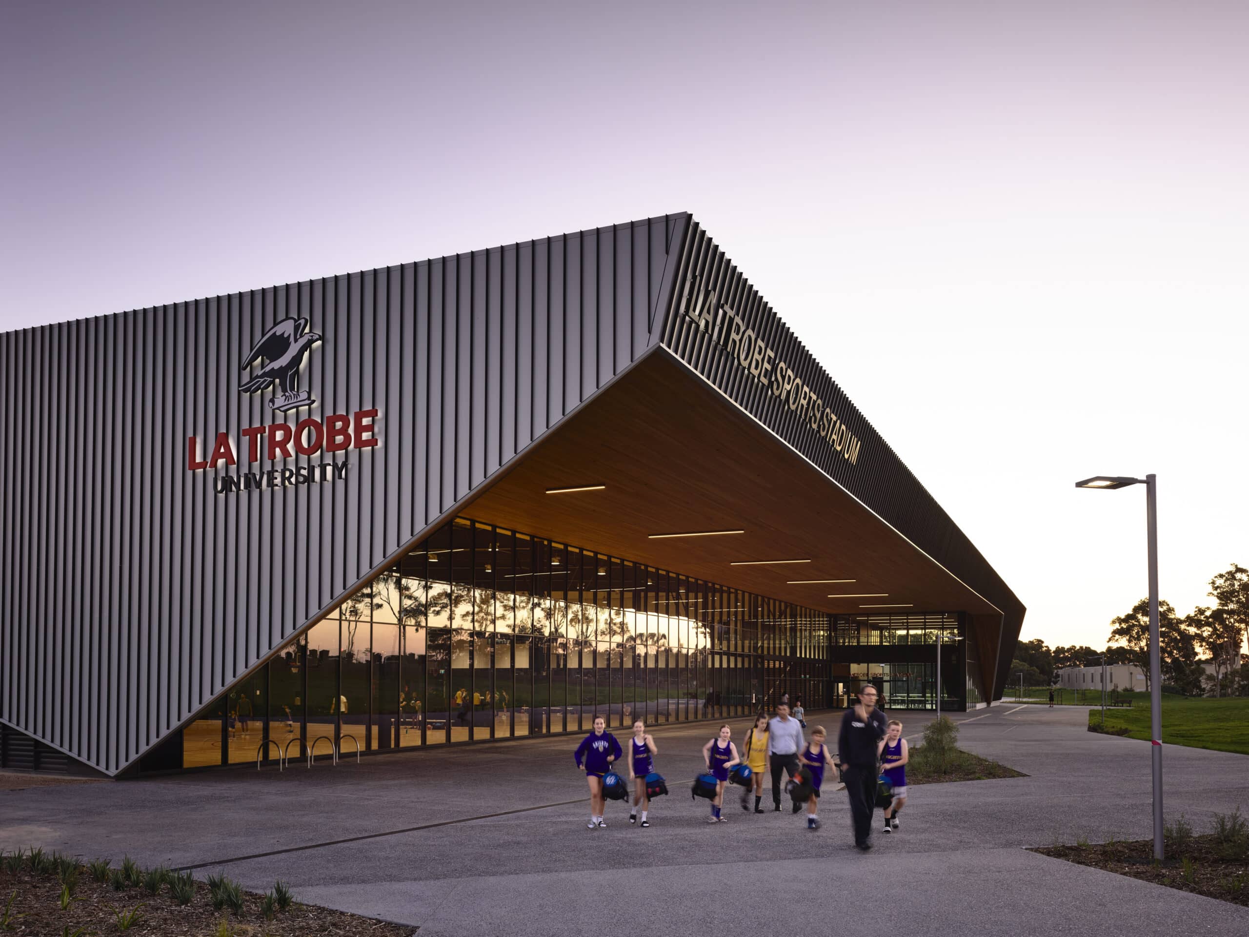 The angular, modern exterior of La Trobe Sports Stadium at La Trobe University, with people walking outside at dusk.