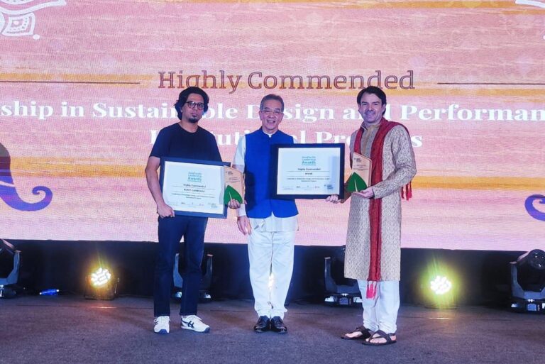 Three men on stage holding certificates and trophies, posing in front of a “Highly Commended” awards backdrop.