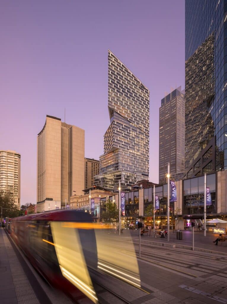 Quay Quarter Tower at dusk with light rail passing and city streetscape in foreground.