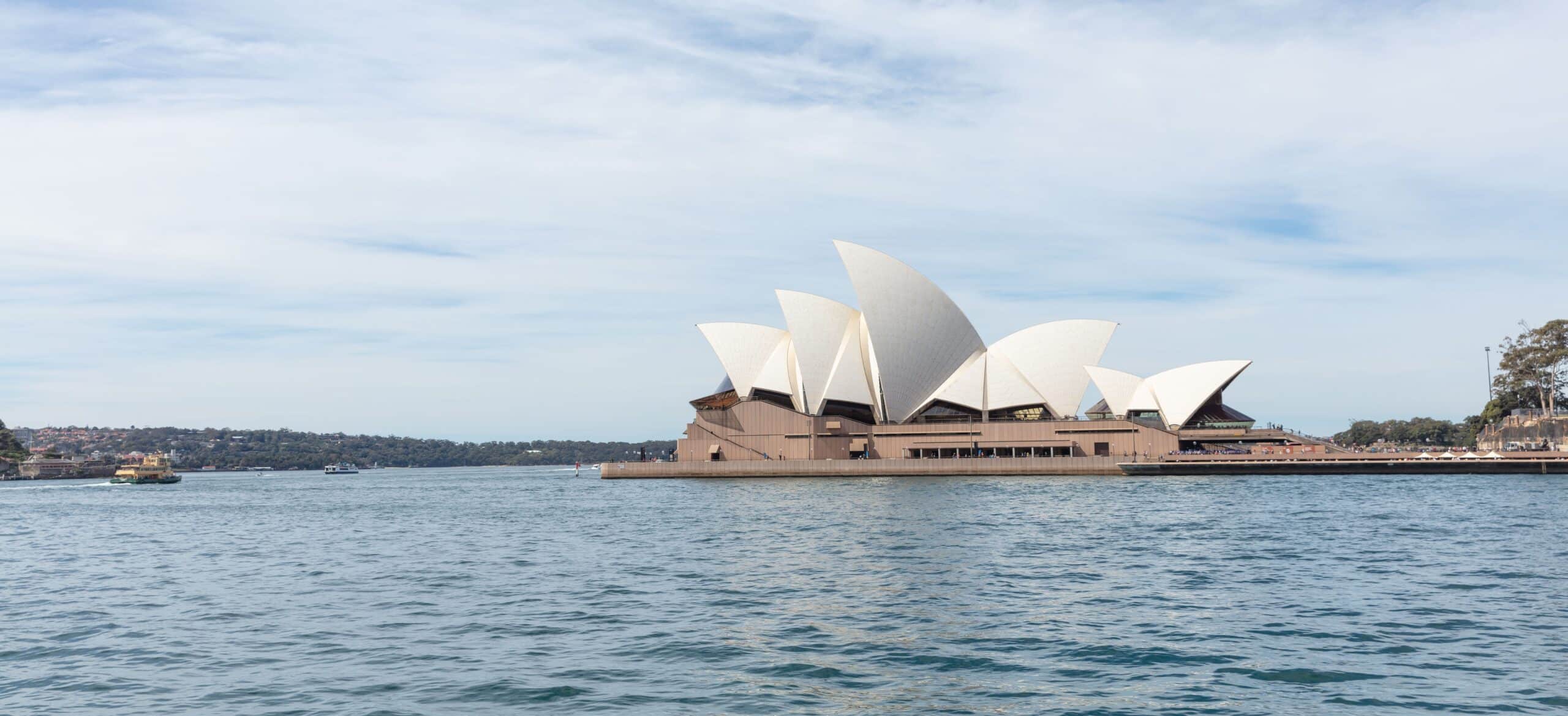 Sydney Opera House on the harbour waterfront with boats and a wide sky overhead.