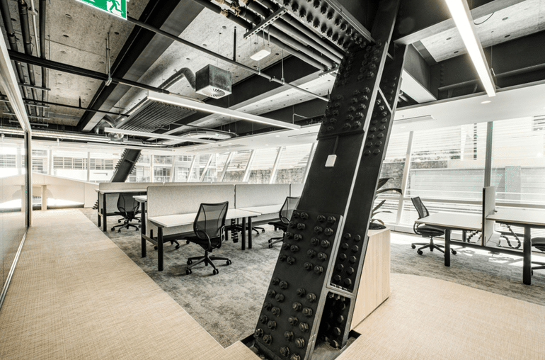 Modern open‑plan office with exposed ceiling, steel column, and workstations by large windows