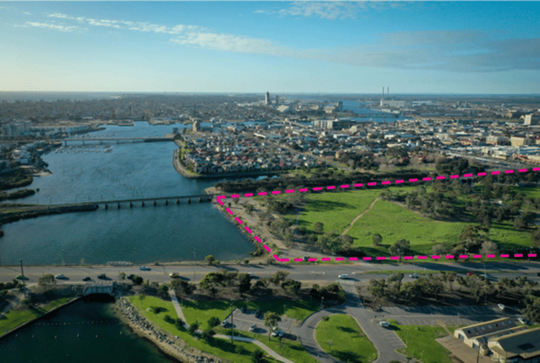 Aerial view of riverside site outlined in pink adjacent to urban and parkland areas
