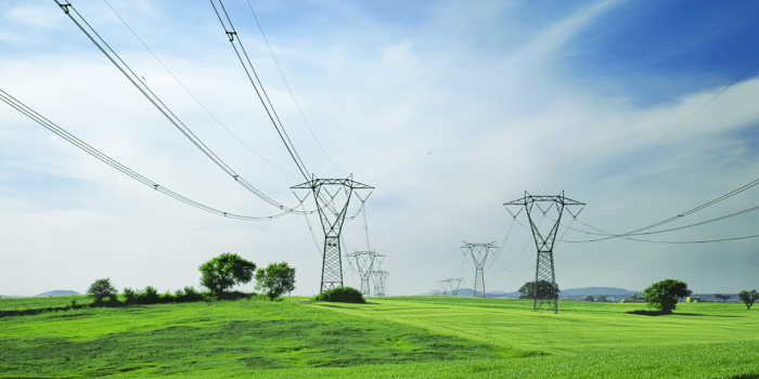 Electric tower wires running through a green field with a blue sky