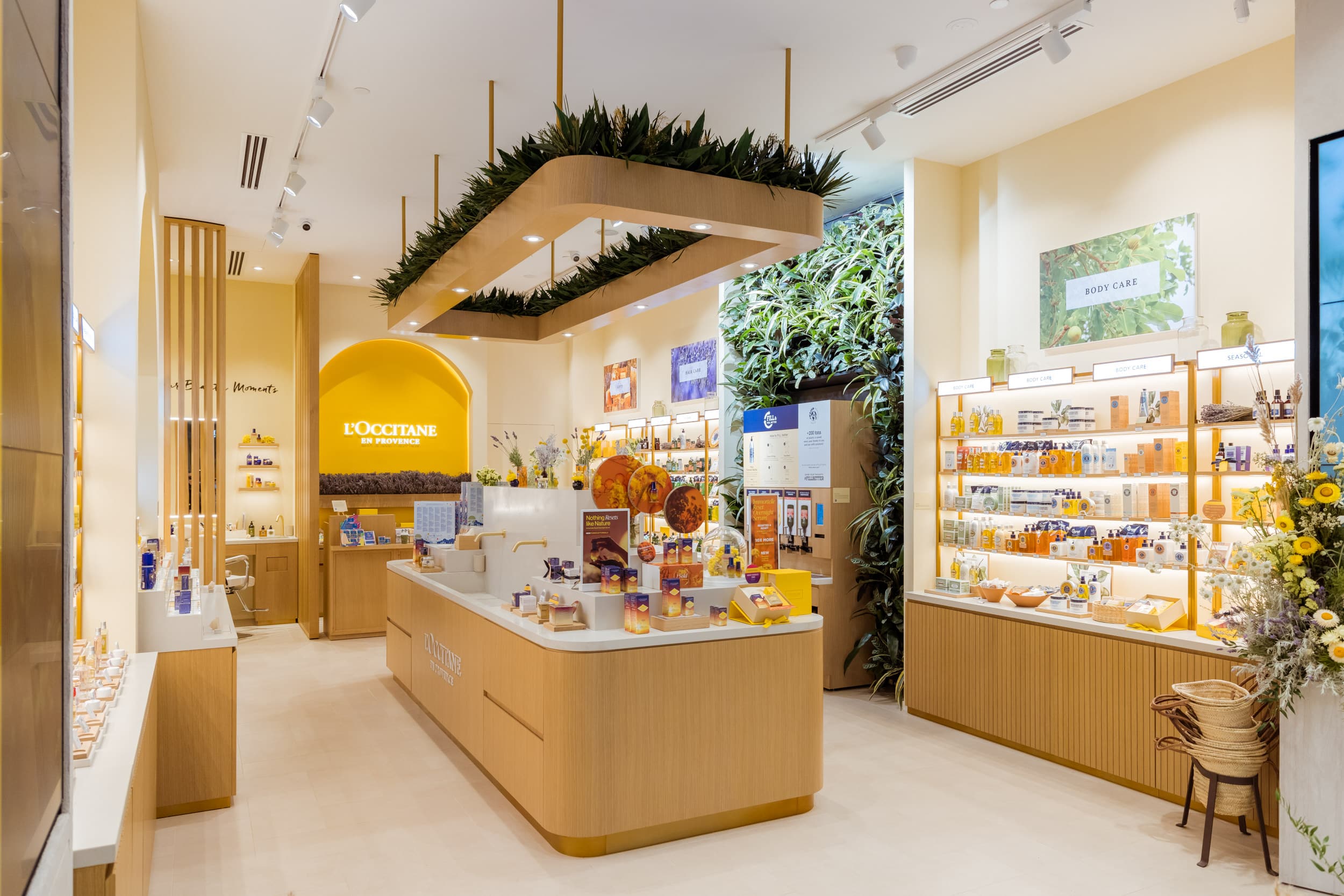 Bright L’Occitane retail store interior with natural wood shelving, green wall and product displays.