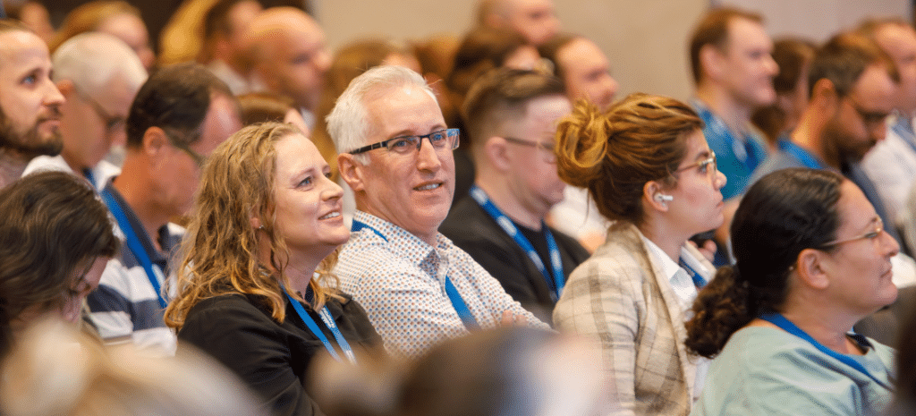 a man and woman sitting in a crowd smiling at a conference